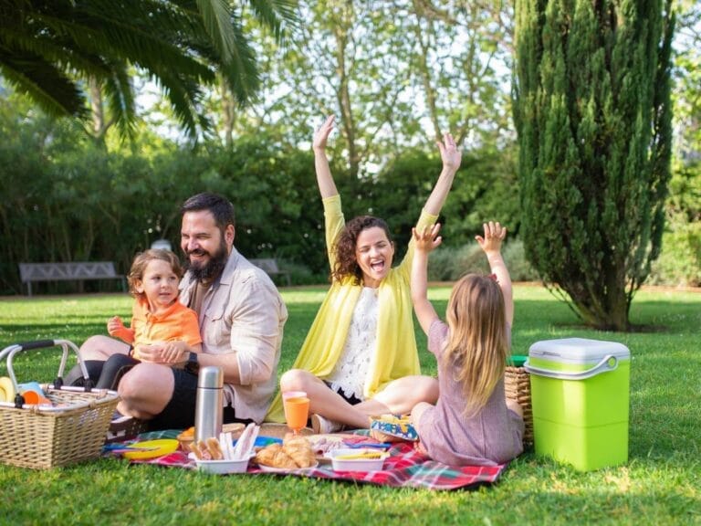 Rodzina z dwojgiem dzieci na pikniku. Obrazek w artykule Przekąski na piknik. Pomysły i przepisy na proste jedzenie.