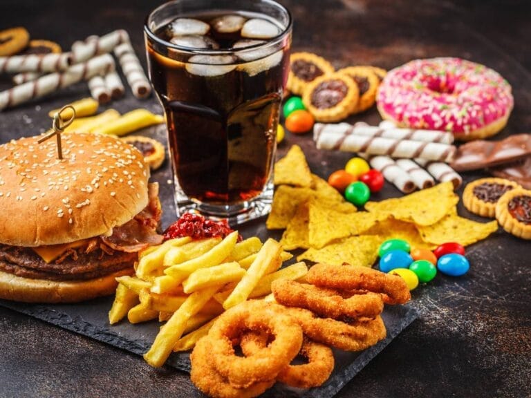 Szklanka coli, hamburger, krążki cebulowe, słodycze. Obrazek w artykule Śmieciowe jedzenie, czyli co? Jakie są skutki niezdrowego odżywiania?